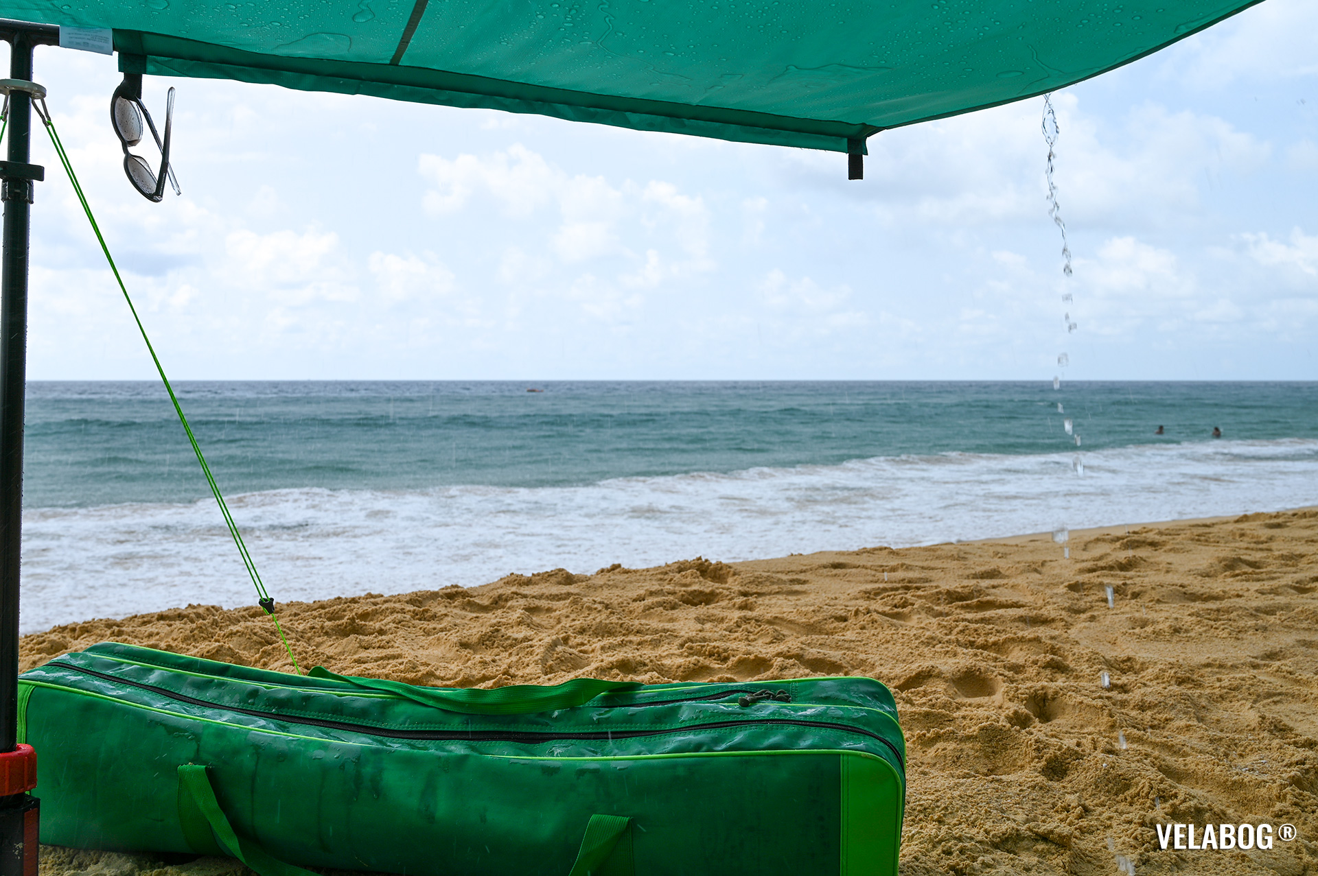 Beach sun sail Velabog Breeze, green, during tropical rain on the beach in Thailand. Best rain and sun shelter on the beach, best beach canopy tent. Setup option for no, light or gusty wind. Bottom view. Details.