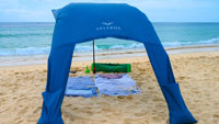 Beach sun sail Velabog Breeze, blue, on the beach with a light breeze. Best beach canopy. Beach sun sail, beach umbrella and beach tent in one. High. Pleasant air circulation. View from behind.