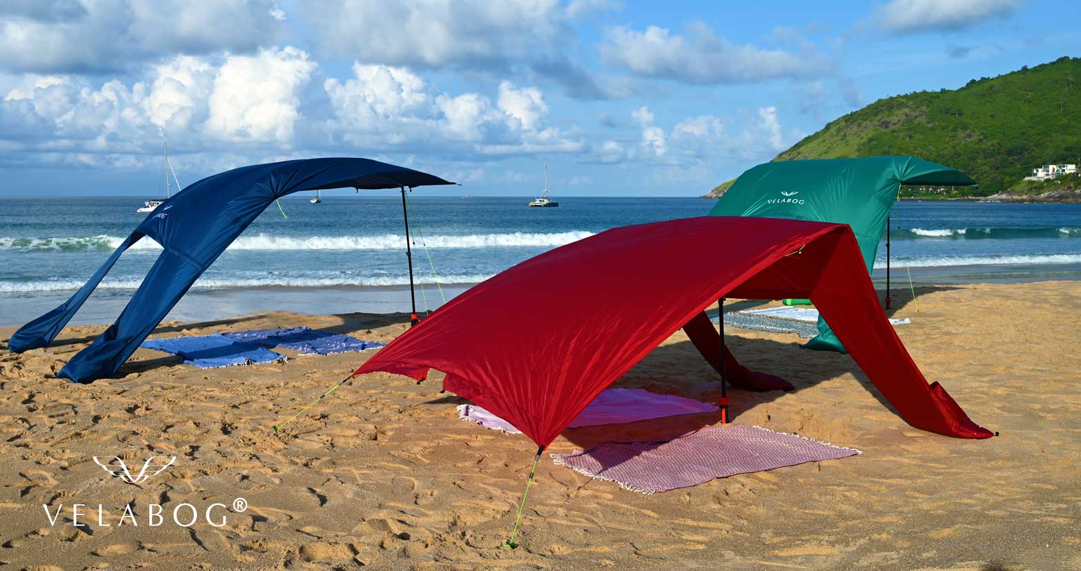Grupa trzech żagli słonecznych Velabog «Breeze» na wietrznej plaży. Doskonała stabilność na wiatr w porównaniu z parasolami i muszlami plażowymi. Różne możliwości konstrukcyjne. Widok z boku.