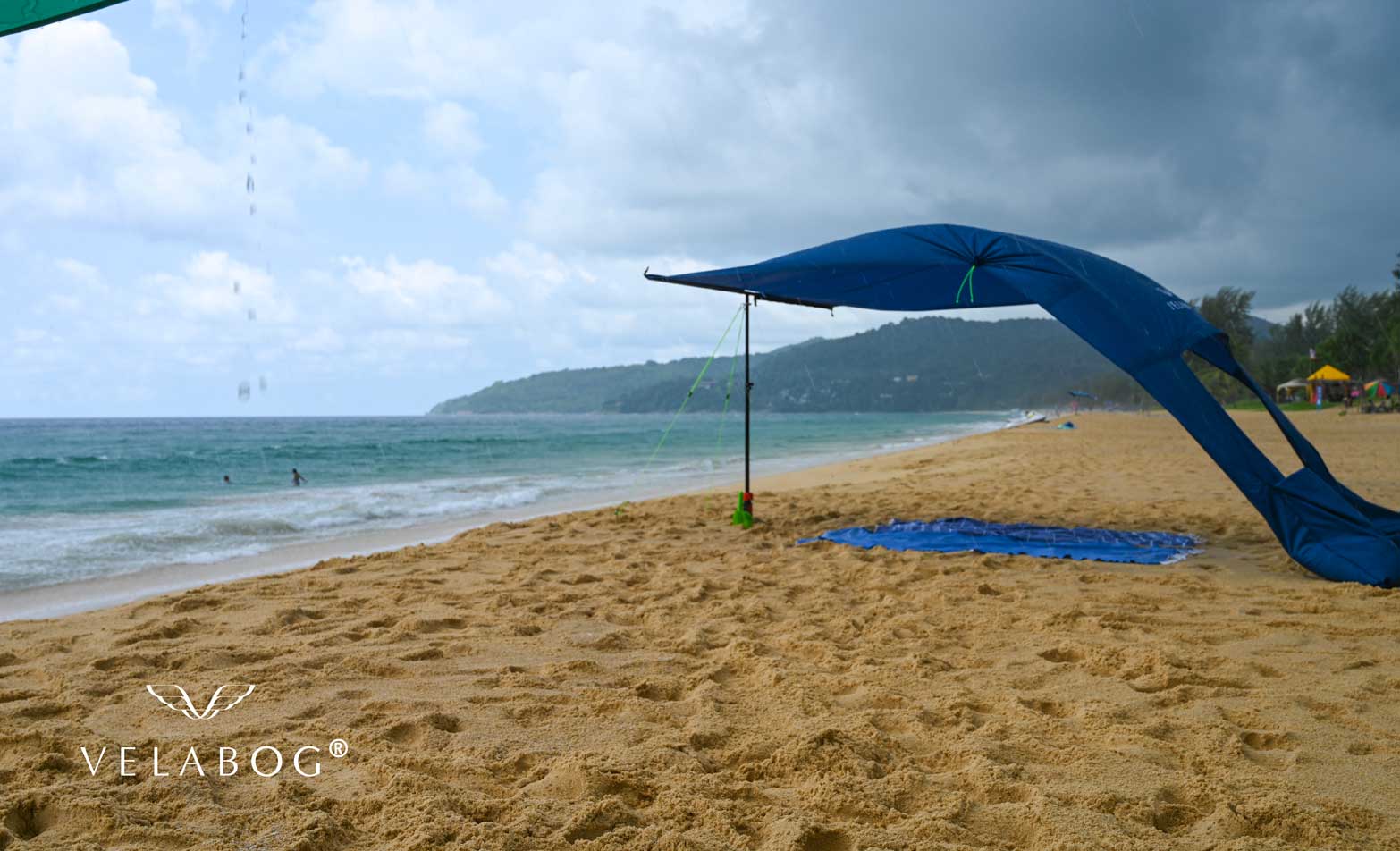 Velabog «Breeze» żagiel słoneczny - ciemnoniebieski. Najlepsza ochrona na plaży przed słońcem nawet podczas deszczu. Może być ustawiony przy lekkim lub silnym wietrze. Widok z boku.