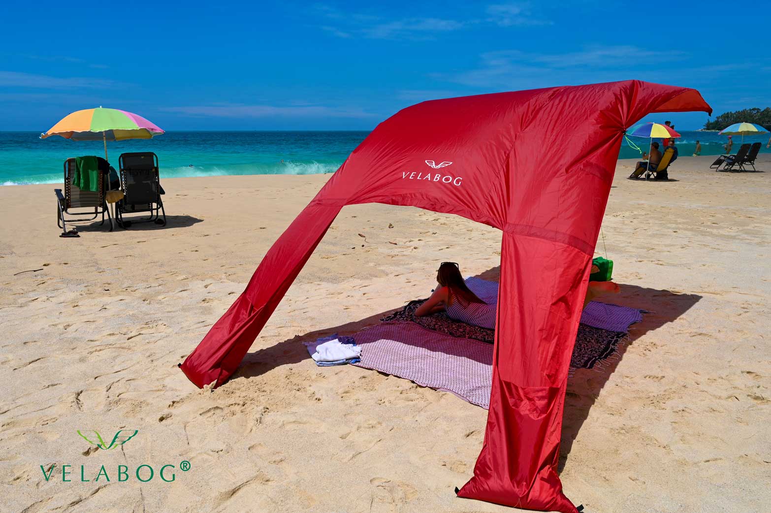 Toldo playa Velabog Breeze rojo. Mucha más sombra en comparación con sombrillas de playa. Mucho más aire en comparación con carpas de playa. Opción de montaje desde viento ligero a fuerte. Sombra generosa.