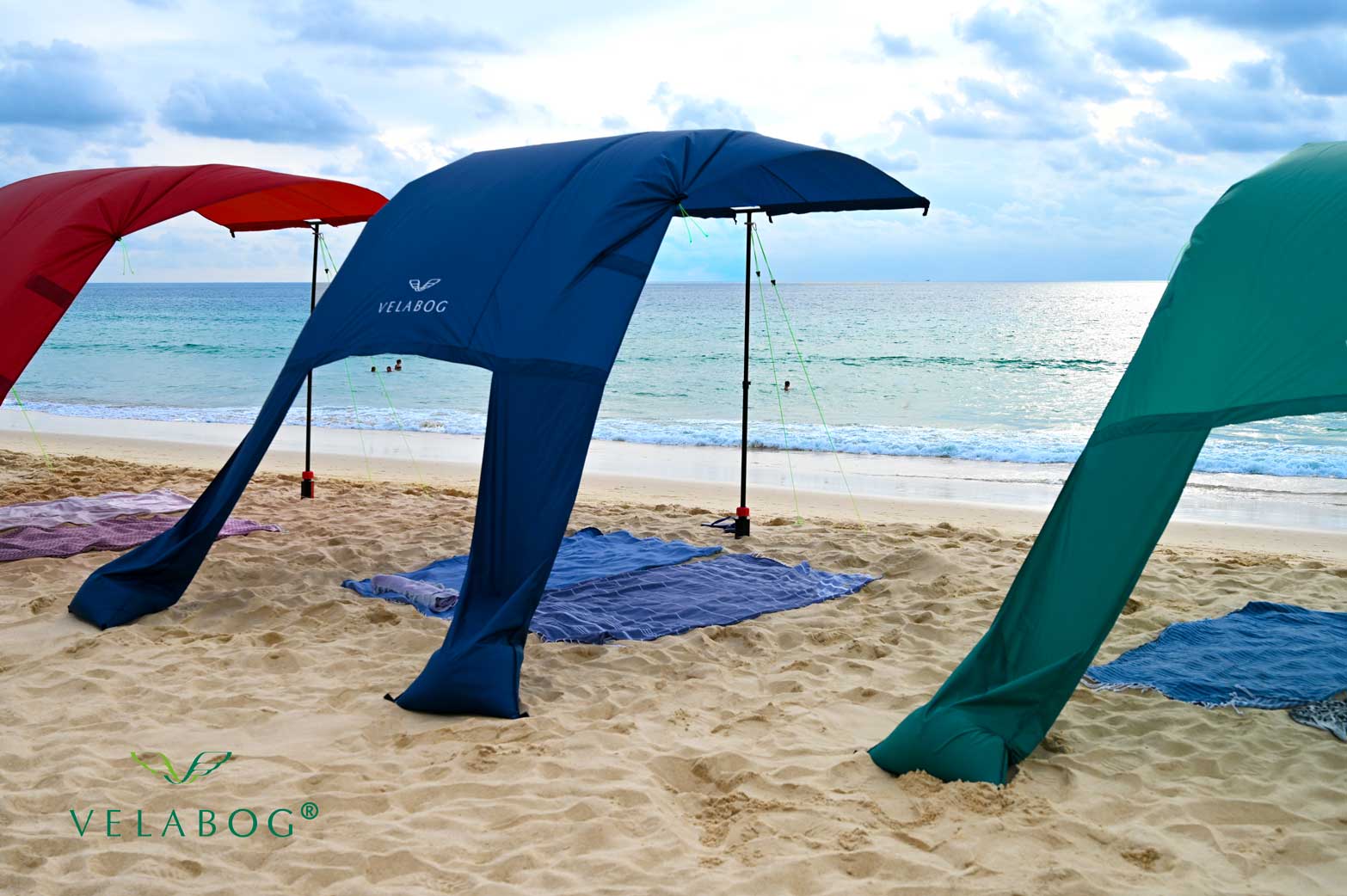 Tres toldos playa Velabog Breeze. La mejor refugio y protección solar para la playa en días de viento. Excelente resistencia al viento en comparación con sombrillas y carpas de playa. Opción de montaje desde viento ligero a fuerte.