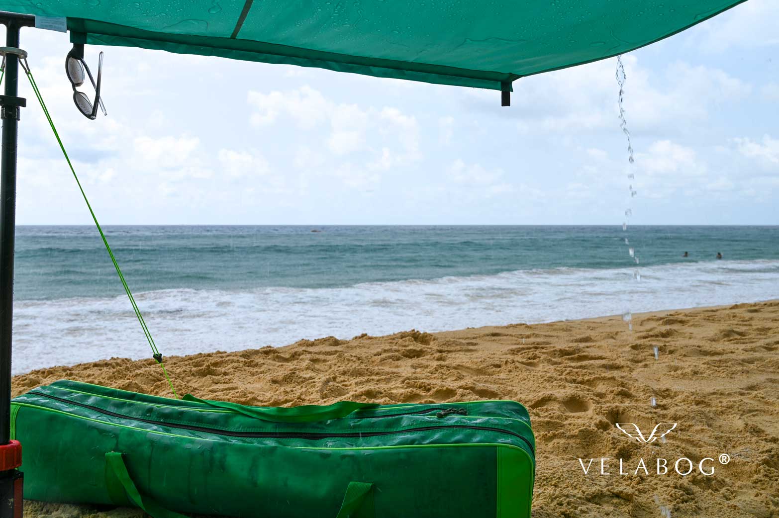 Voile d’ombrage tente plage Velabog Breeze, vert, pendant une averse tropicale sur une plage en Thaïlande. La meilleure protection contre le soleil et la pluie à la plage. Option de montage - pas de vent, vent faible ou vent en rafales. Le meilleur auvent de plage. Vue de dessous. Zoom.