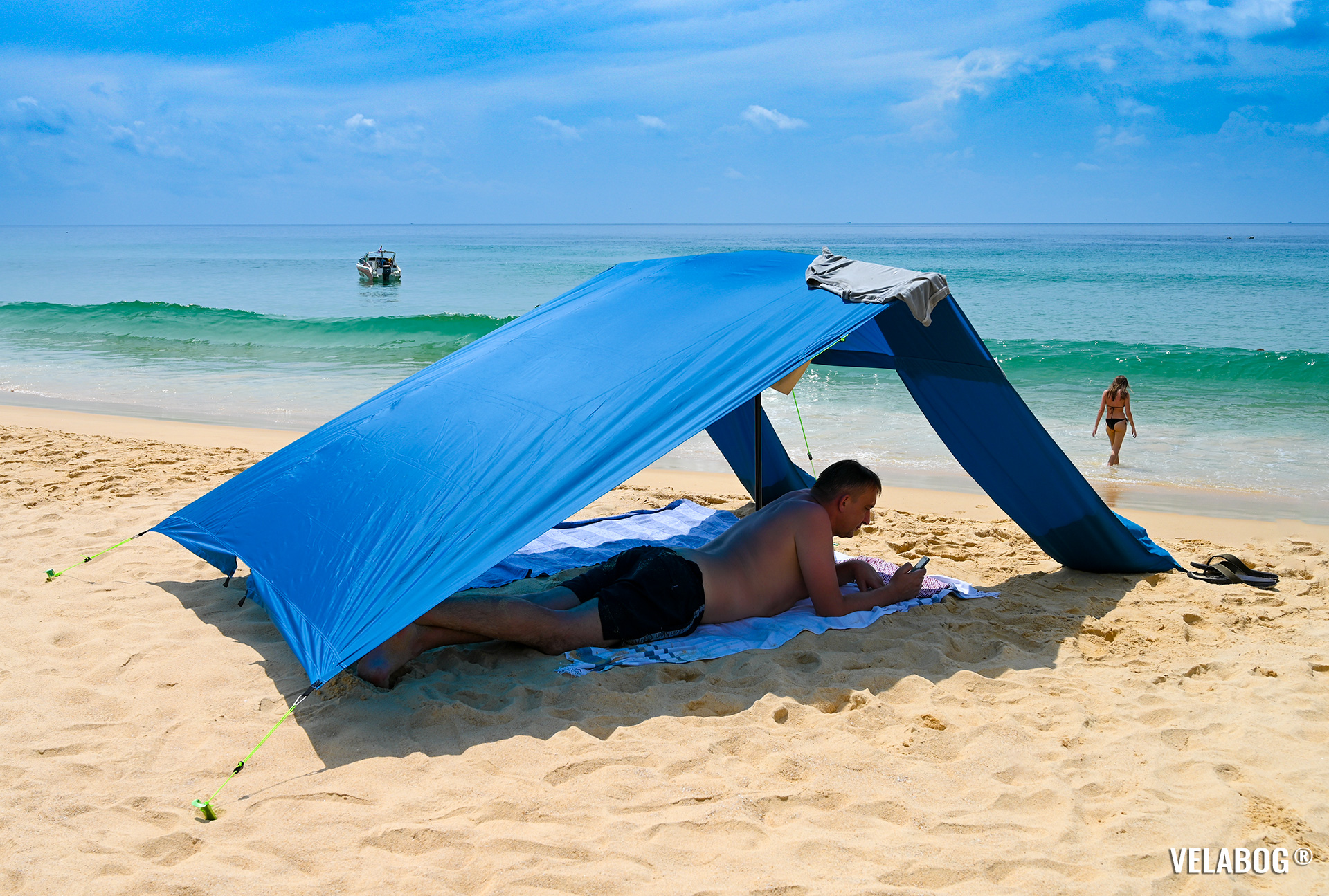 Strand Sonnensegel Strandzelt Velabog Breeze, blau. Luftiger Sonnenschutz am Strand auch ohne Wind. Beste Alternative zu Strandschirmen, Strandzelte und Strandmuscheln. Test Strand Sonnensegel Aufbauoption - kein, leichter oder böiger Wind. Ansicht von der Seite. Personen.