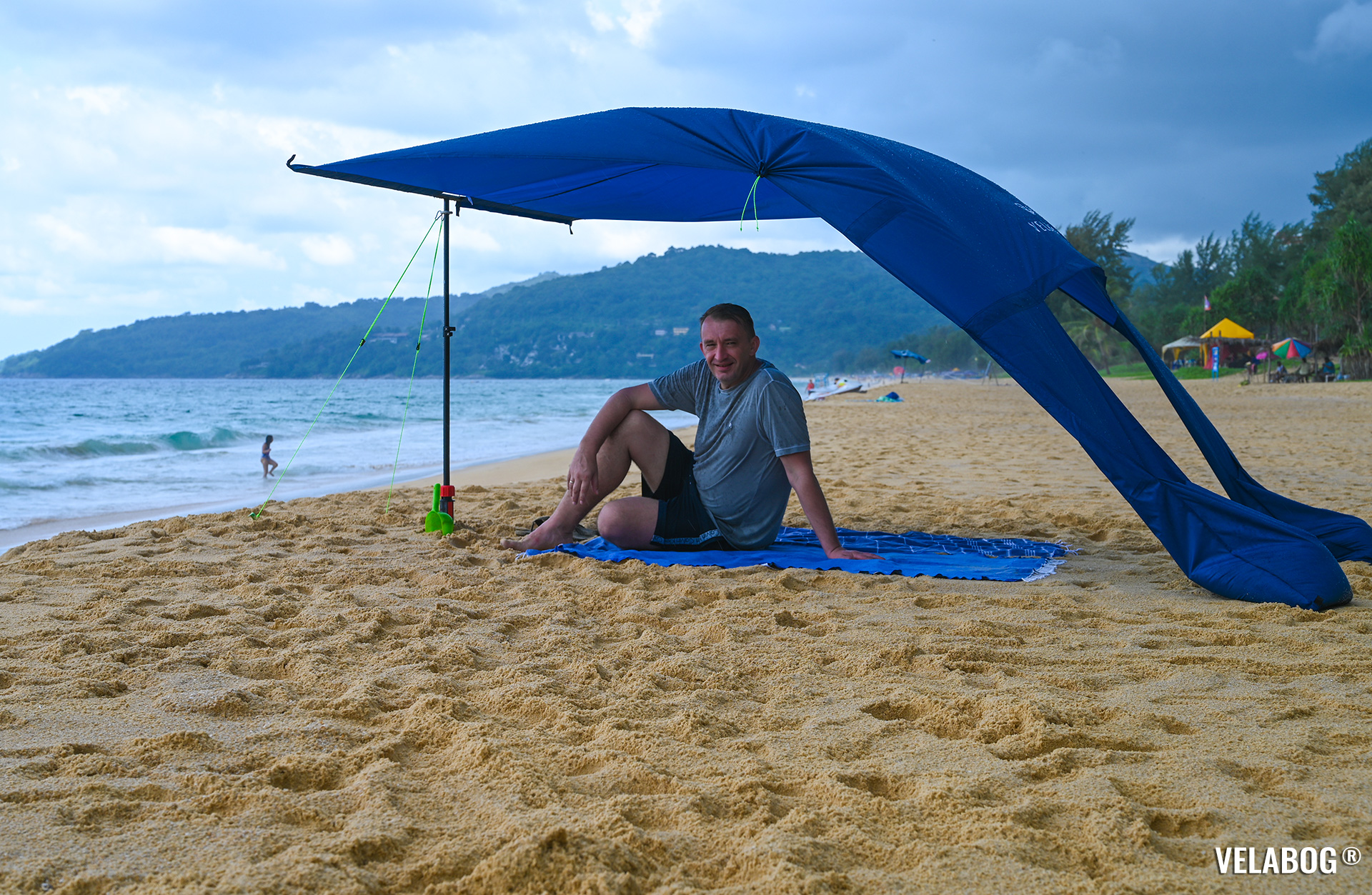 Strand Sonnensegel Strandzelt Velabog Breeze, nachtblau. Bester Sonnenschutz Strand. Test in Thailand auch bei einem Regenschauer. Beste Alternative zu Strandschirmen, Strandzelten und Strandmuscheln. Aufbauoption beim leichten bis starken Wind. Ansicht von der Seite. Personen.