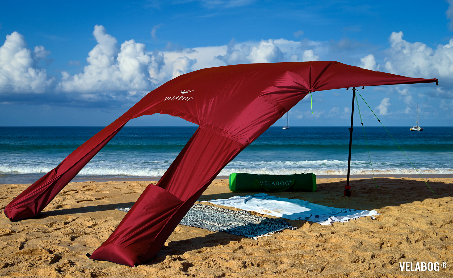Strand Sonnensegel Strandzelt Velabog Breeze, rot. Bester Sonnenschutz Strand. Stylisch, luftig, schattig. Test Strand Sonnensegel Aufbauoption beim leichten bis starken Wind. Windstabil. Ansicht von schräg hinten.