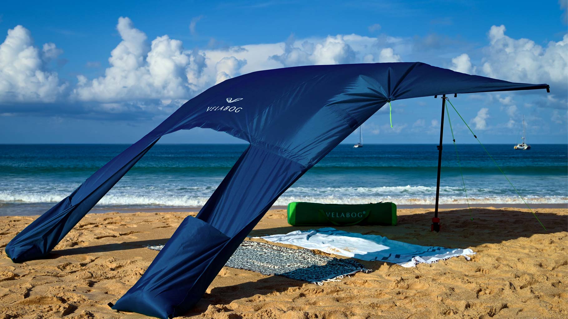 Vela da sole tenda spiaggia Velabog Breeze, blu notte, sulla spiaggia ventosa. Vela da sole, ombrellone e tenda da spiaggia in uno. Molto ampia e pur sempre compatta. Miglior tettoia da spiaggia. Vista obliqua dal retro.