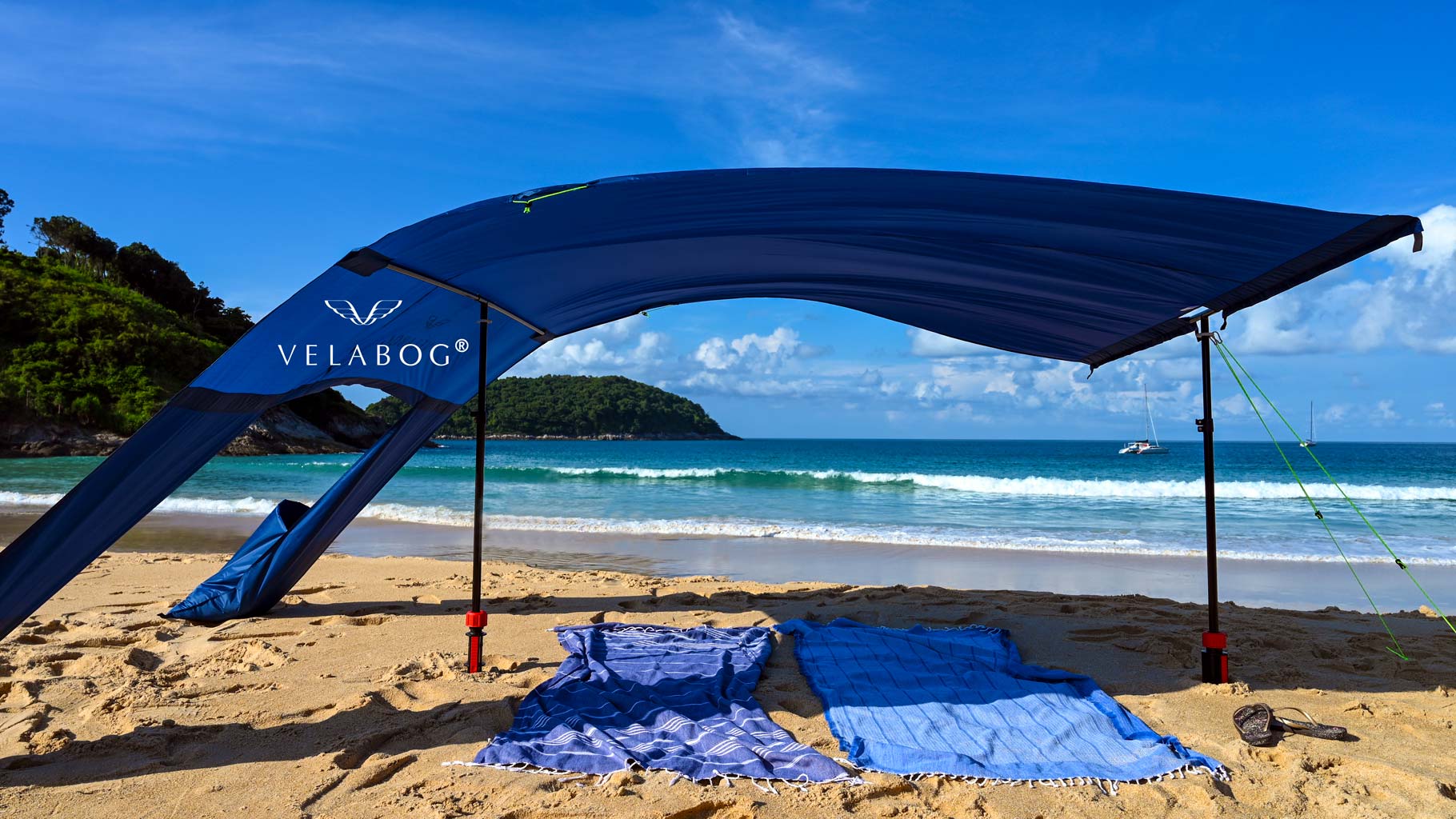 Voile d’ombrage tente plage Velabog Breeze bleu nuit avec kit d’extension sur une plage balayée par des rafales de vent. Voile d’ombrage, parasol et tente de plage en un seul produit. Offre beaucoup d’ombre par tout type de vent, qu’il soit faible, fort ou en rafales. Vue de dessous.