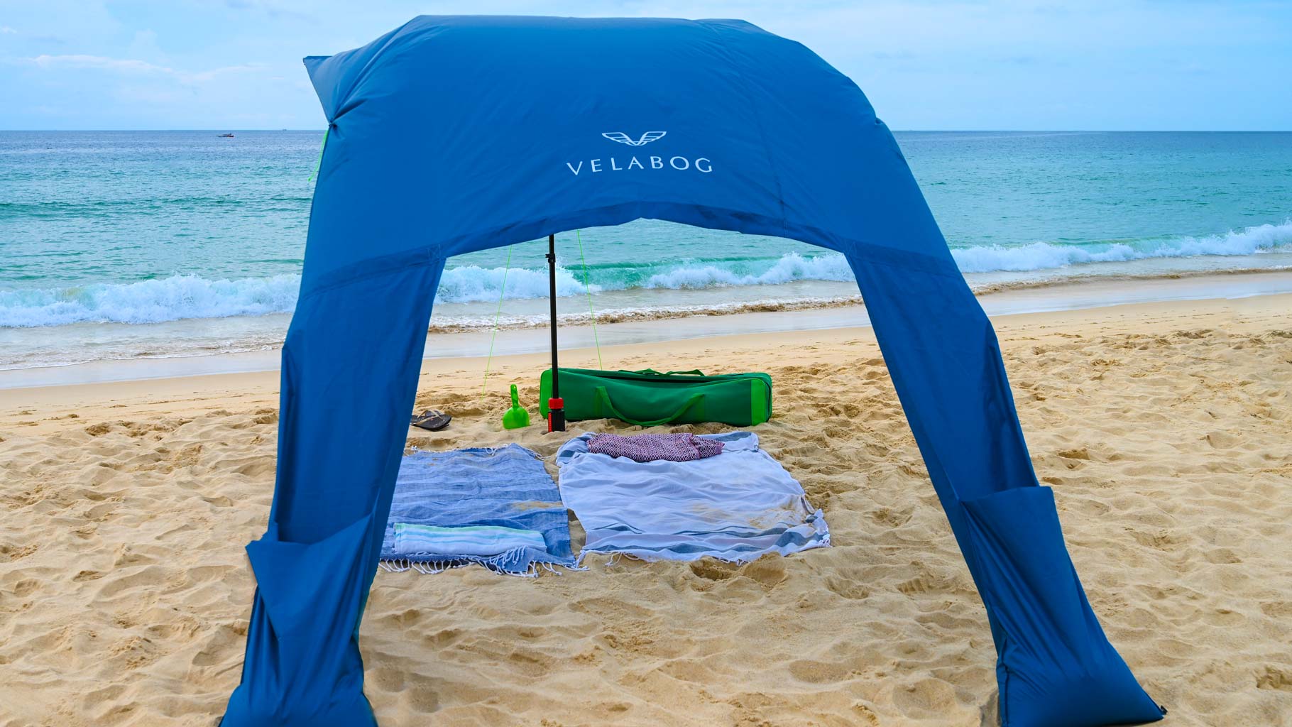 Żagiel słoneczny namiot plażowy Velabog Breeze, niebieski, na plaży przy lekkim wietrze. Żagiel słoneczny, parasol plażowy i namiot plażowy w jednym. Wysoko. Bez akumulacji ciepła. Najlepsze zadaszenie na plażę. Widok od tyłu.